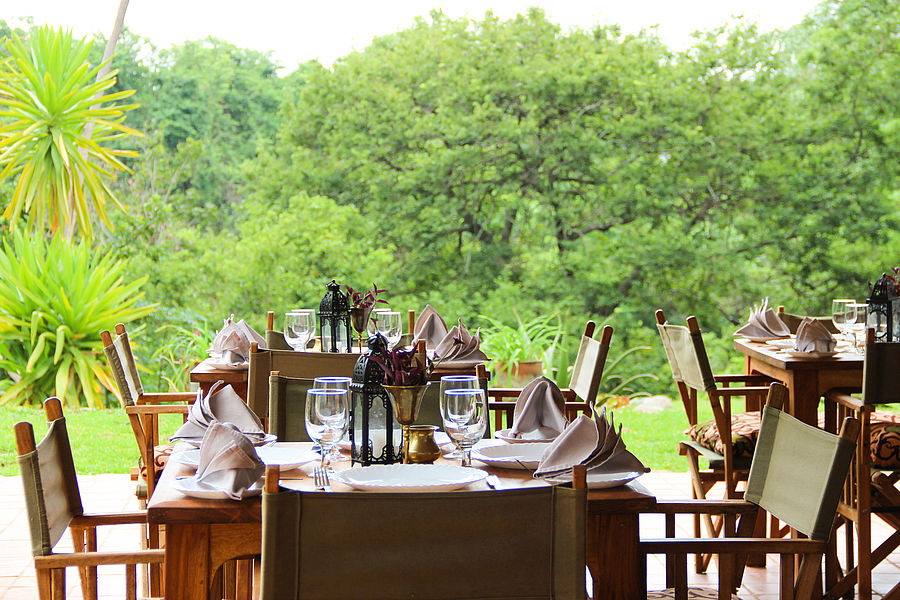 Chairs at tables with cutlery, glasses, napkins in front of a green forest