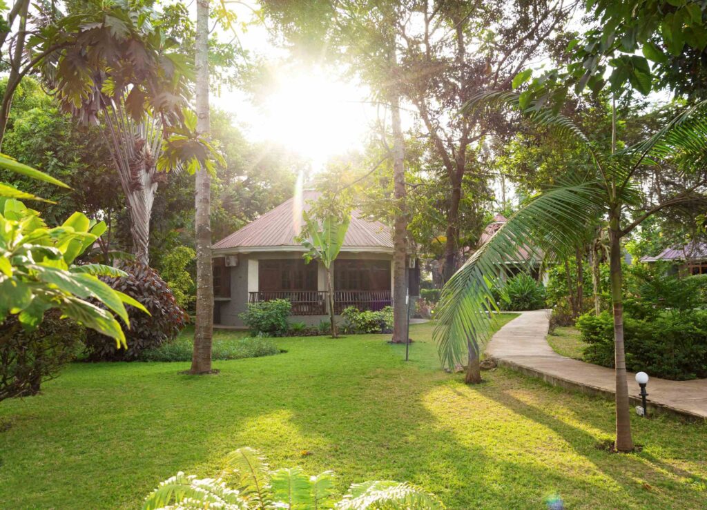 Arusha Planet Lodge garden with round bungalows, green lawn and palm trees