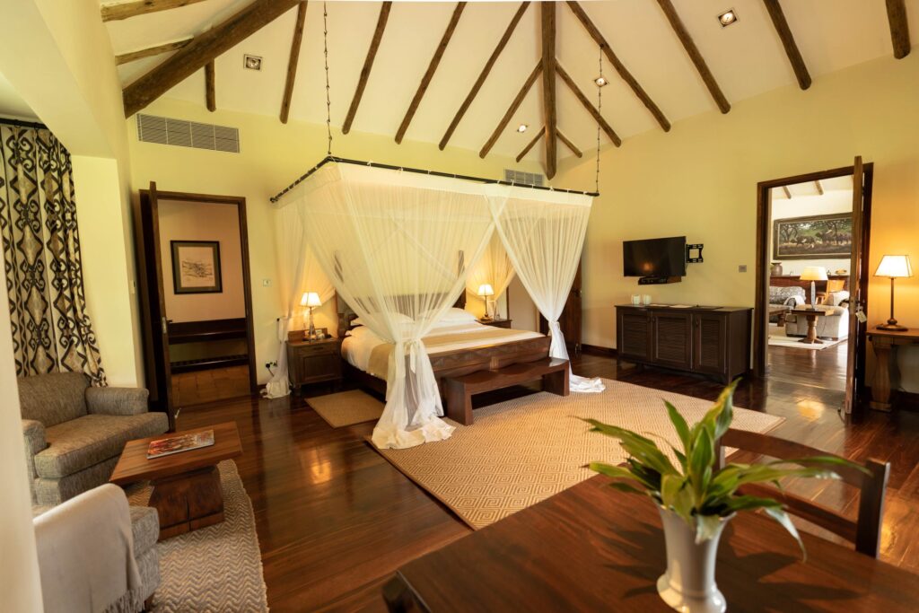 Room with a wooden bet with a mosquito net, grey armchairs and a bright carpet