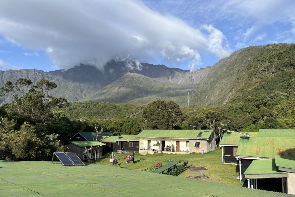 Miriakamba Huts of Mount Meru with green roof surrounded by the mountain, trees and green fields