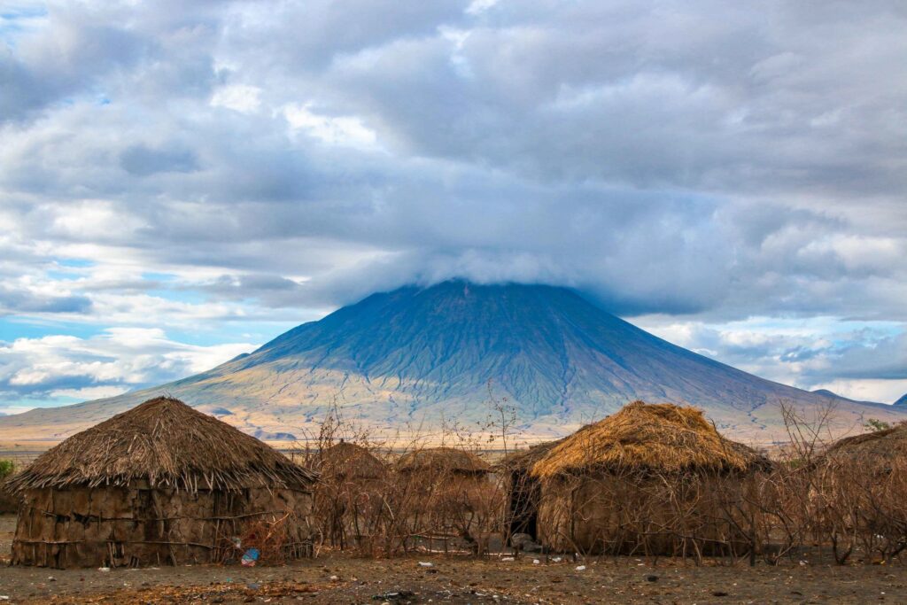 Ol Doinyo Lengai in the clouds with straw huts in front