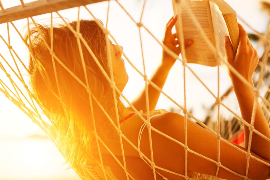 Woman lying in a hammock in the sunlight reading