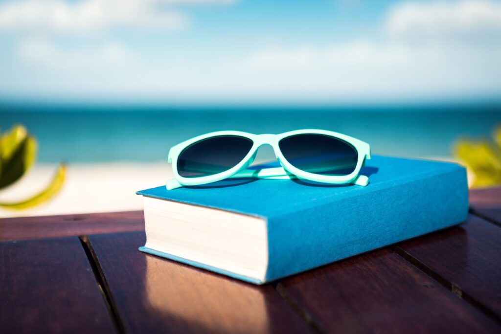 A book and sunglasses on a table with the beach in the background