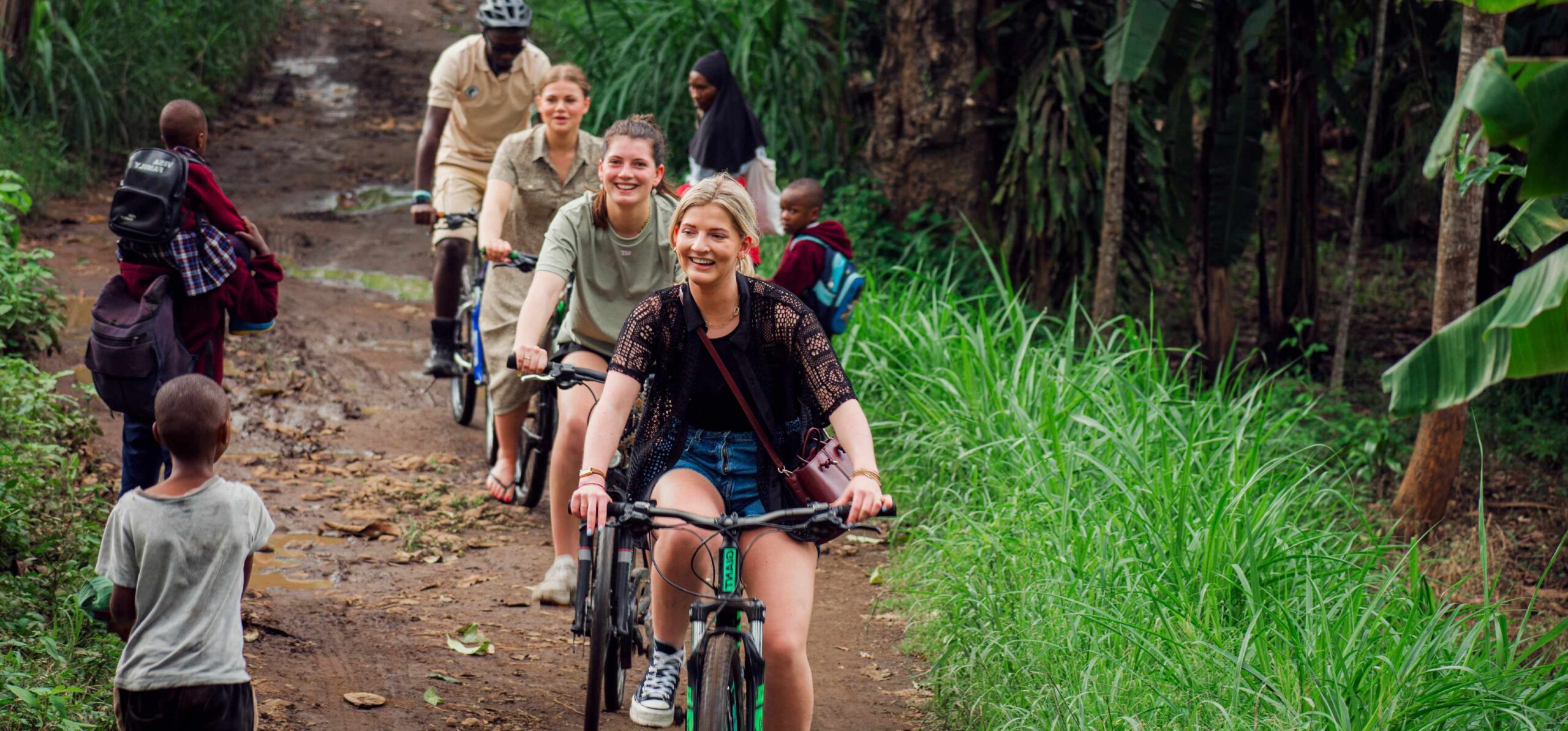 Four people biking on a trail in a forest with kids standing at the trail