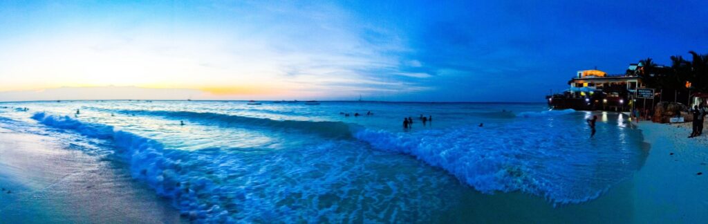 Strand von Nungwi, Tansania, bei Sonnenuntergang mit großen Wellen und Menschen, die im Meer schwimmen