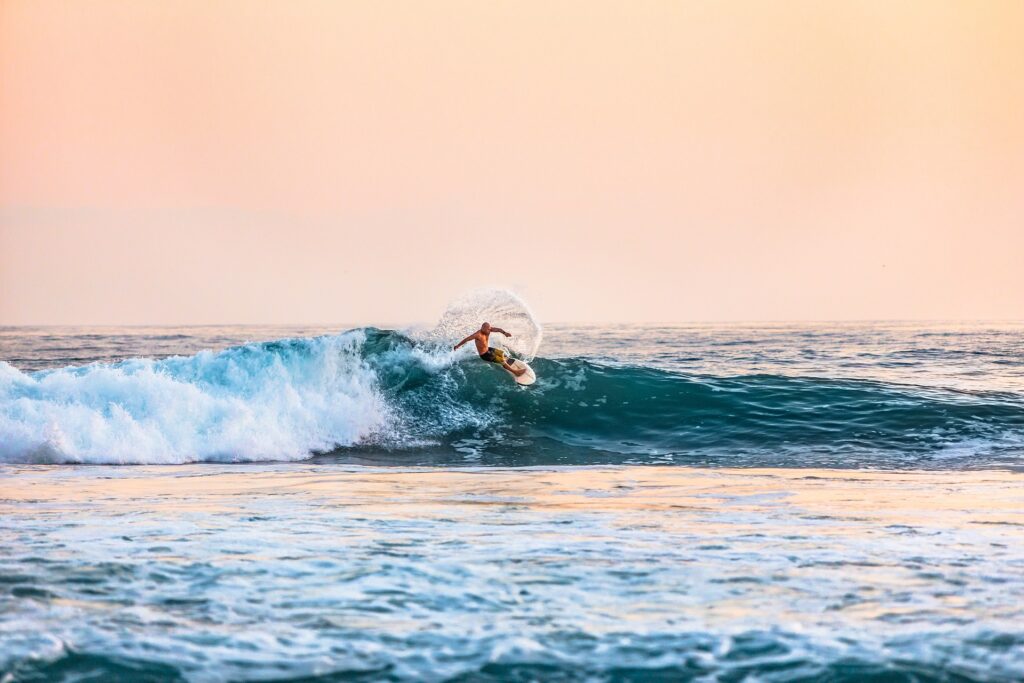 Homme surfant sur une vague au coucher du soleil