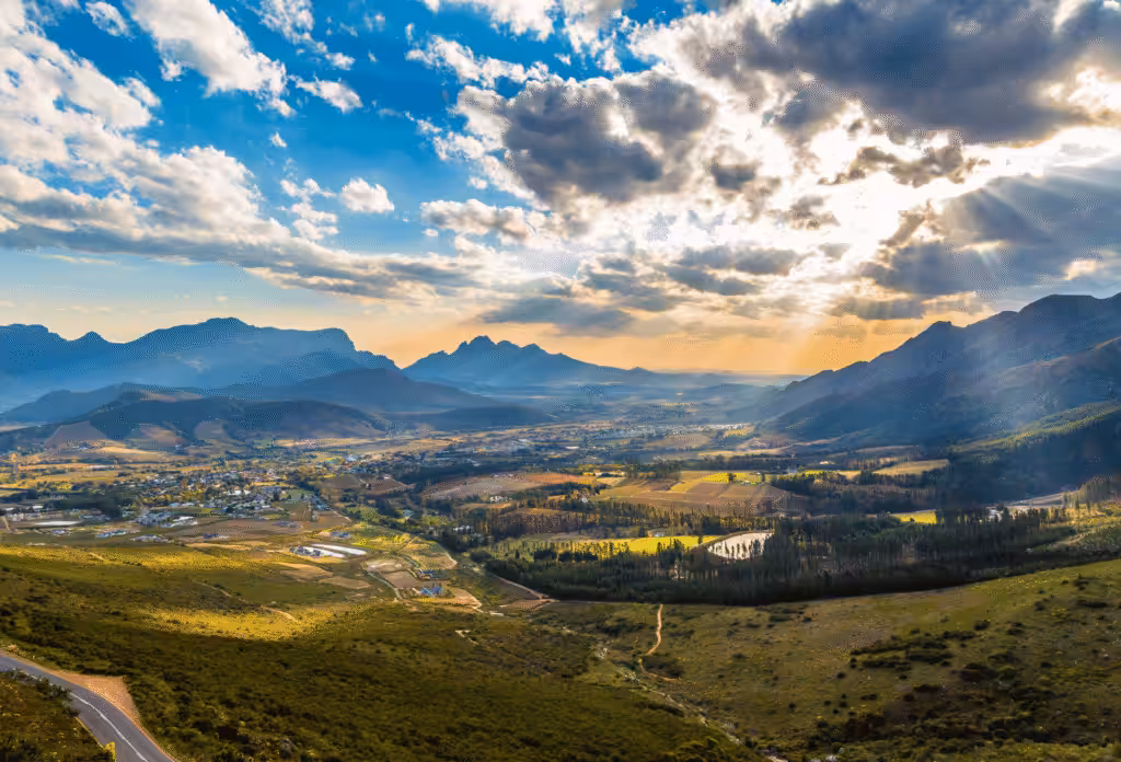 The landscape of Franshhoek in South Africa from above, with mountains in the background and the sun shining through darker clouds