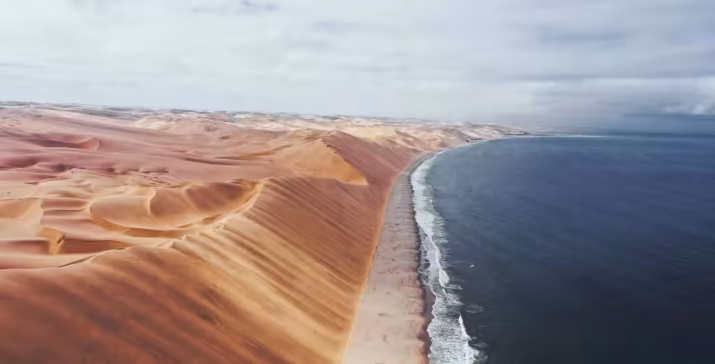 Sandwich Harbour in Namibia from above, with high dunes on the left, a beach in the middle and the ocean on the right